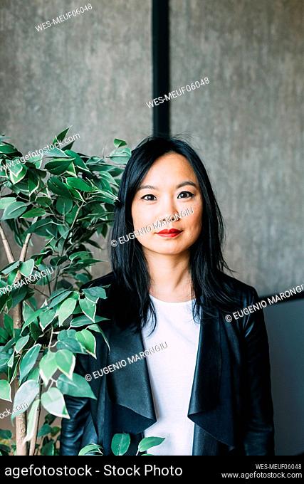 Confident businesswoman by plant at office