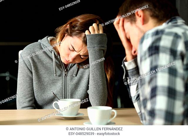 Sad couple of teenagers complaining sitting in a bar in the night