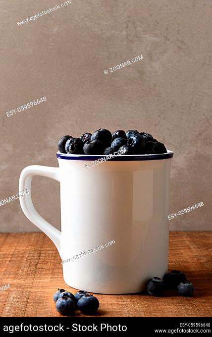 Blueberry Still Life. A white mug filled with fresh picked Blueberries on a wood table. Vertical format with copy space