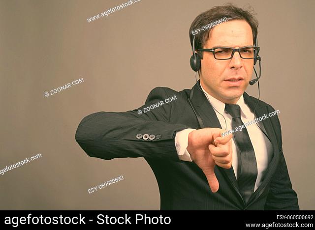 Studio shot of handsome Persian businessman working as call center representative against gray background
