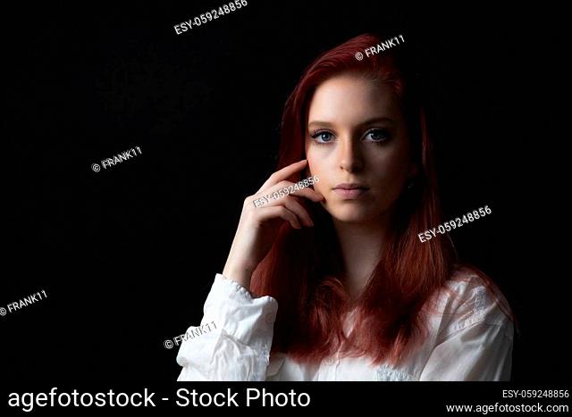 Low key portrait of beautiful young woman touching her face looking at the camera. Horizontally