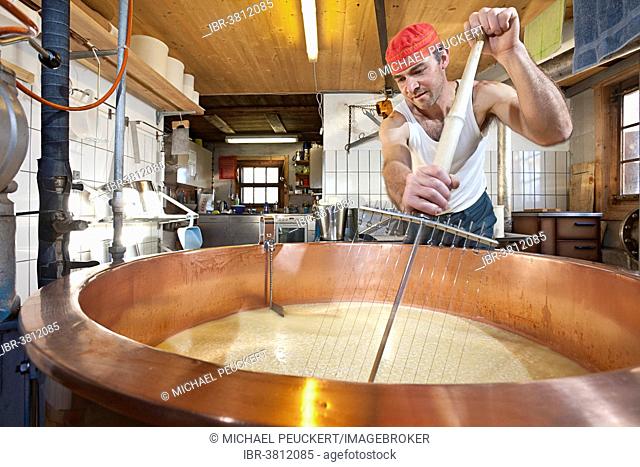 Dairyman mixing the whey and the curd with a cheese harp in a copper kettle, Alp Gün, Graubünden, Switzerland