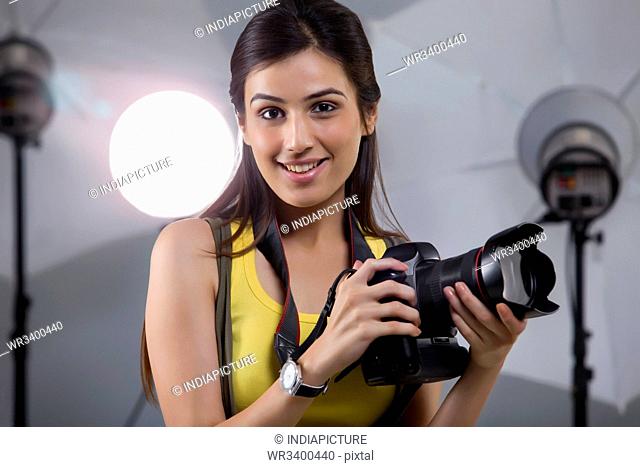Close-up of young female photographer with digital camera in studio