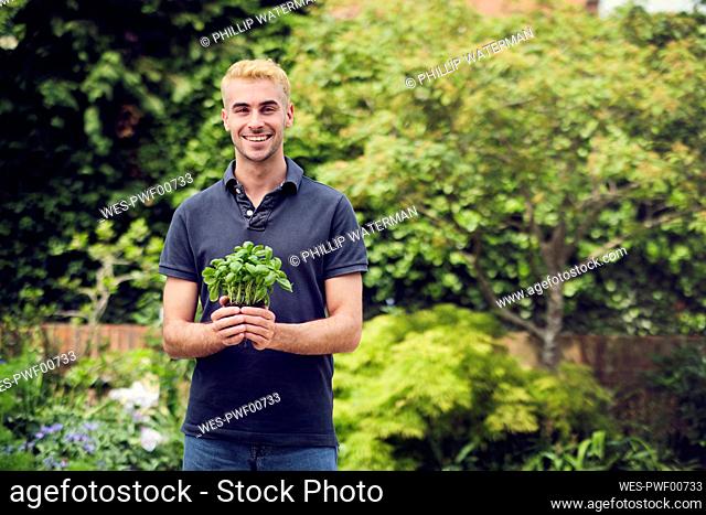 Smiling young man holding plant at back yard