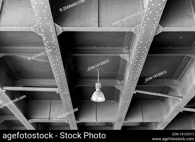 A lonely lamp hangs under the bridge in black and white