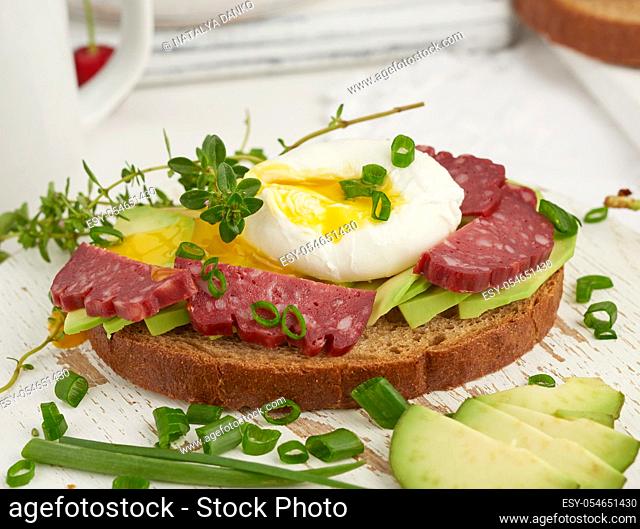 toast with poached egg and avocado on a round board, morning breakfast, top view on a white table