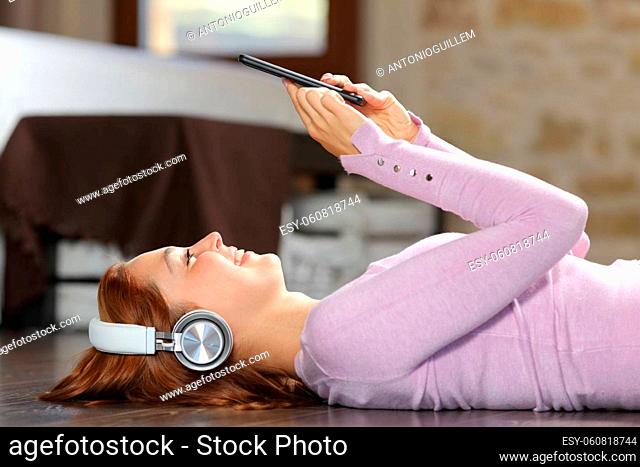 Side view portrait of a happy woman listening to music lying on bedroom at home