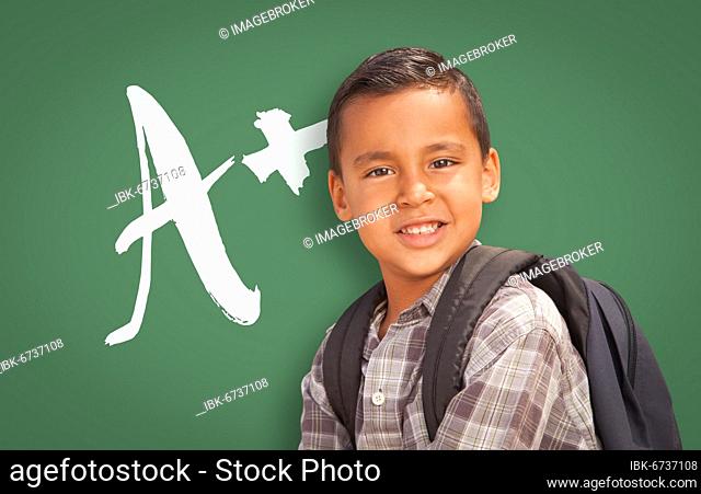 Cute hispanic boy in front of A+ written on chalk board