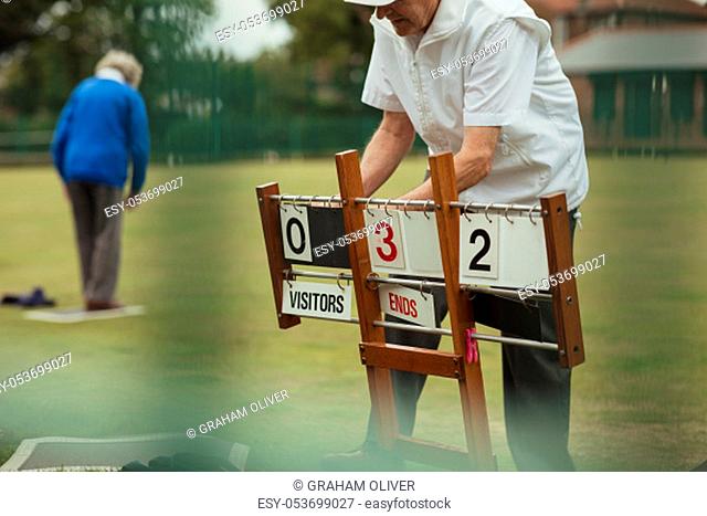 A senior man at a bowling green setting up the scoreboard