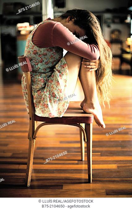 Teenager girl with a country flowers dress seating with the legs on top of the chair and head in his arms thoughtfully fitness