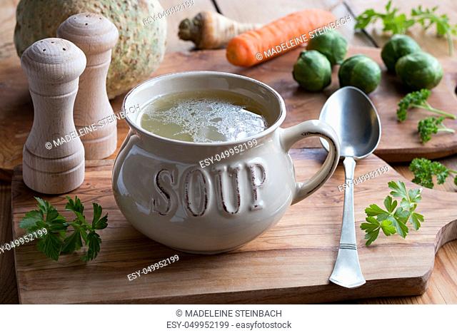 Bone broth made from chicken in a soup bowl, with vegetables in the background