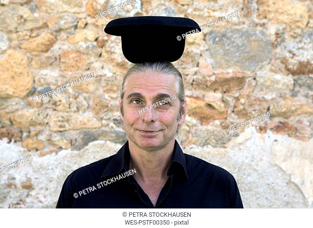 Portrait of man at stone wall balancing a bowler hat on his head
