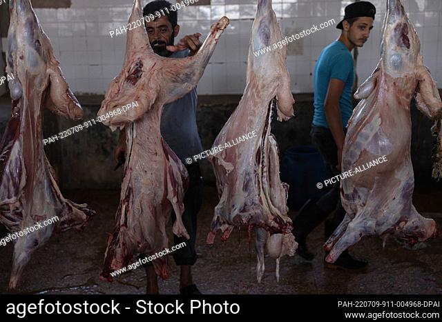 09 July 2022, Syria, Idlib City: Syrian workers slaughter and flay sacrificial sheep inside a slaughterhouse as part of a ritual followed by Muslims during Eid...