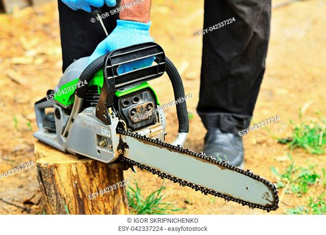 A man in blue working gloves launches a chainsaw to spray a log, a close-up photo