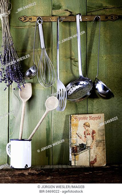 Old cookbook with cooking utensils in front of a green wooden wall