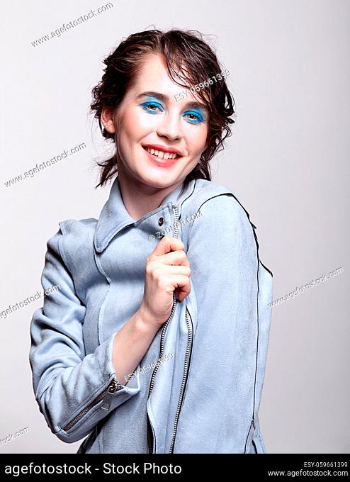 Portrait of smiling female in blue jacket. Woman with unusual beauty makeup and wet hair. Girl with perfect skin, green pistachio colour eyes and blue shadows...