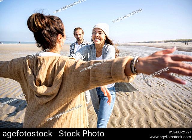 Woman with arms outstretched to hug daughter with men in standing in background at beach