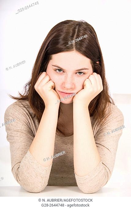 Unhappy sulking teenage girl, elbows on table, had between hands