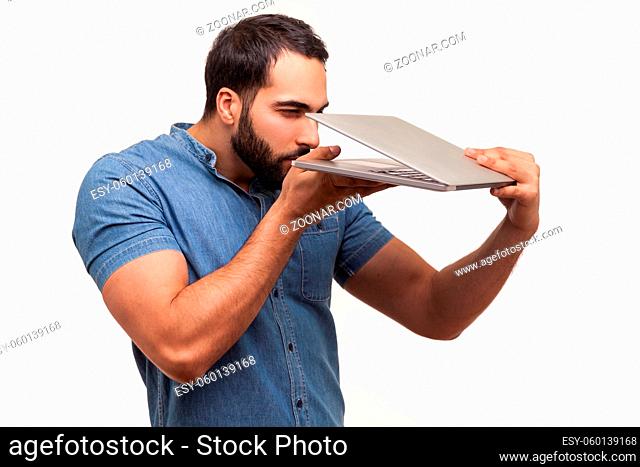 Curious nosy man with beard in blue shirt peeping inside opened laptop, trying to see private information, spying. Indoor studio shot isolated on white...