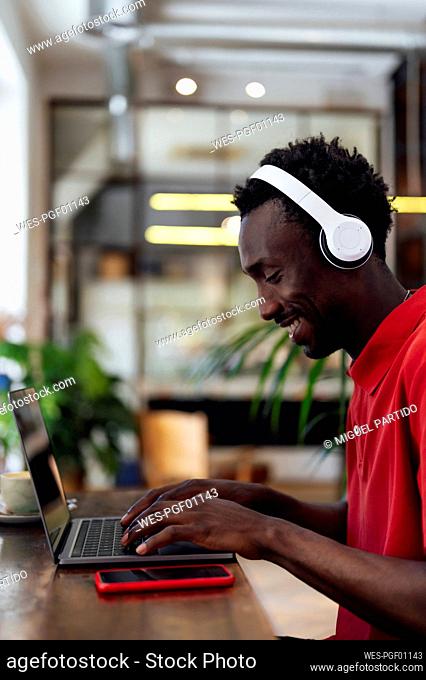 Smiling man wearing wireless headphones using laptop