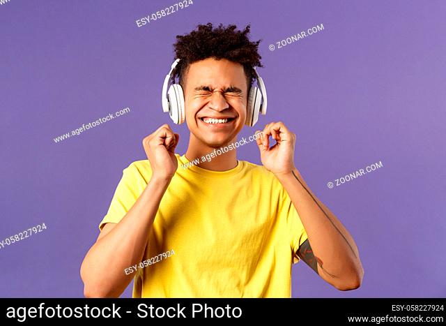 Portrait of pleased, excited young man enjoying nice quality awesome beats in headphones, close eyes and smiling rejoicing, dancing over cool new song