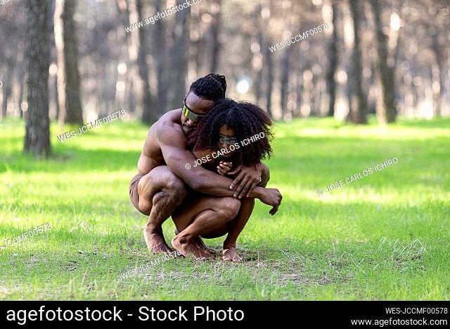 Two professional dancers wearing futuristic goggles crouching and embracing in middle of forest
