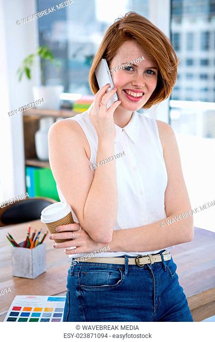 smiling hipster business woman sitting on her desk on the phone