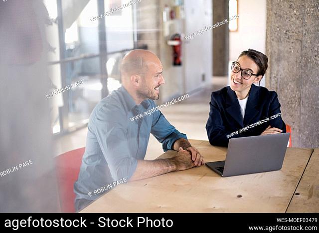 Smiling business people using laptop while sitting at office