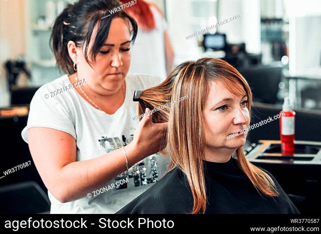 Hairdresser styling dyeing combing womans hair. Young woman working as a hairdresser in hair salon. Real people, authentic situations