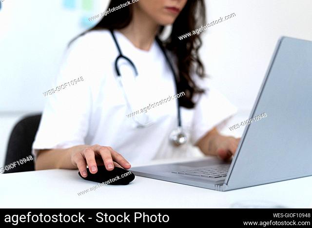 Young female doctor taking online consultation through laptop in clinic