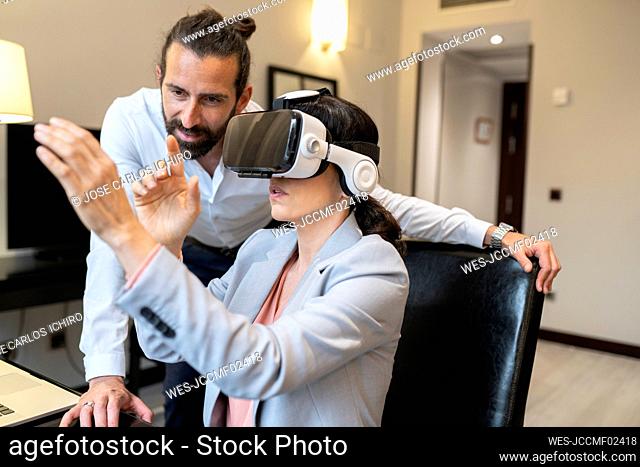 Mature businesswoman wearing virtual reality simulator by male colleague in hotel