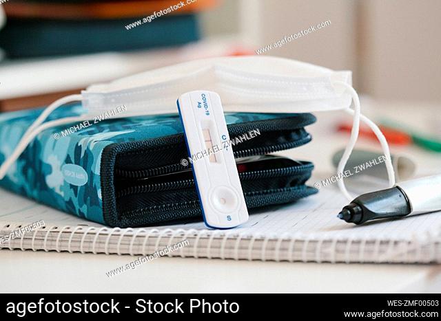 Rapid diagnostic test kit with protective face mask over pencil case at desk in school