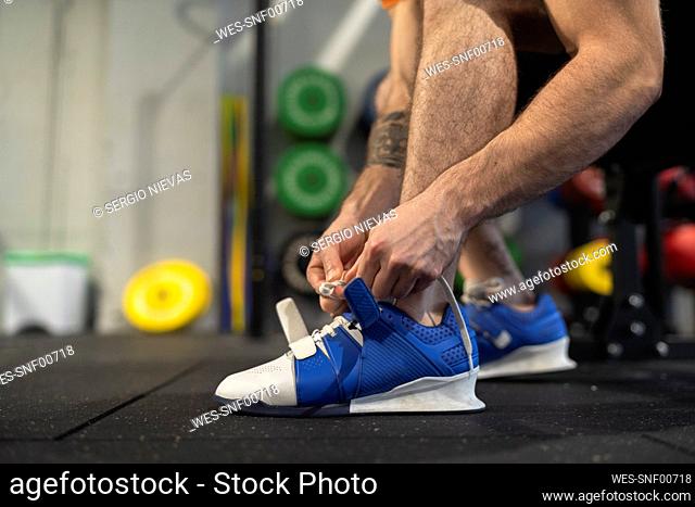 Male athlete tying shoelace while sitting in gym