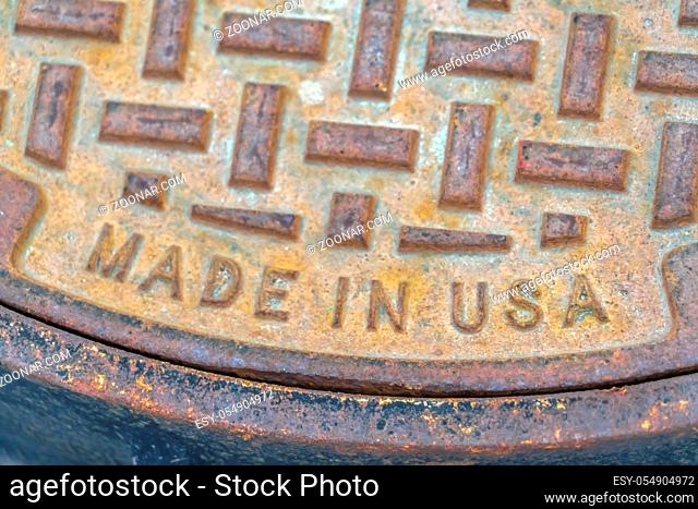 Round and rusty manhole cover made in USA. Close up view of a round and rusty manhole cover on a road in Utah Valley. The weathered manhole cover is made in the...