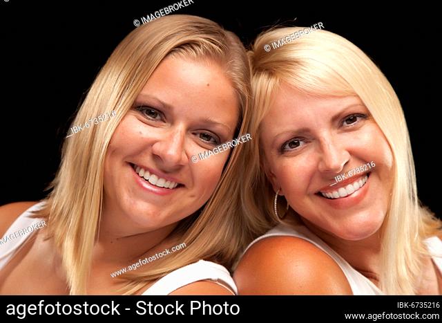 Two beautiful smiling sisters portrait isolated on a black background