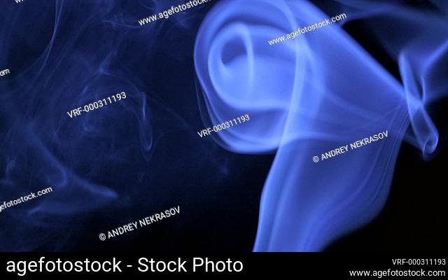 Thin trickle of bright neon blue smoke slowly rising graceful twists up on black background. Colored smoke blowing from bottom to top. Closeup