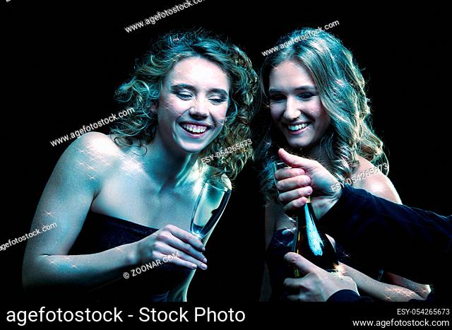 Two girls with glasses of champagne in their hands. Beautiful young women with vogue shining sparkle face makeup. Female Christmas portrait cinematic blue toned