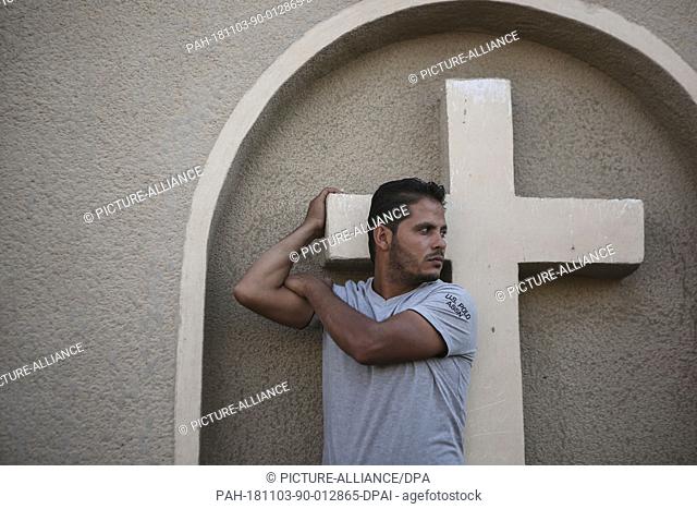 03 November 2018, Egypt, New Minya: A man holds onto a cross at the Coptic graves during the funeral of the victims who were killed during a gun attack on a bus...