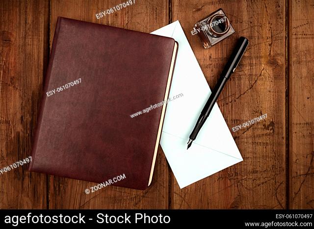 An overhead photo of a leather bound journal, a blue envelope, an ink well and pen, shot from above on a dark rustic background with a place for text