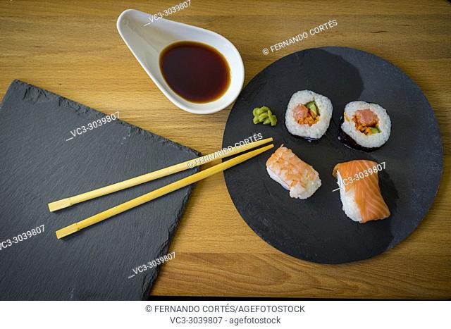 Sushi on a wooden table on black slate plate with soy sauce and chopsticks