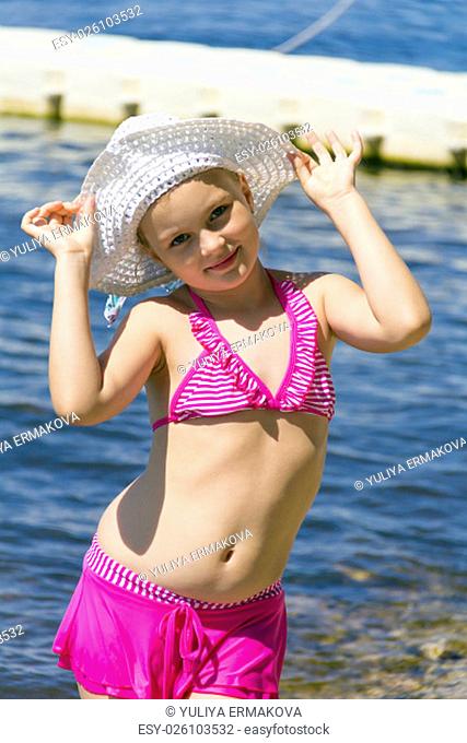 Dancing girl on the riverbank in pink swimsuit and white hat
