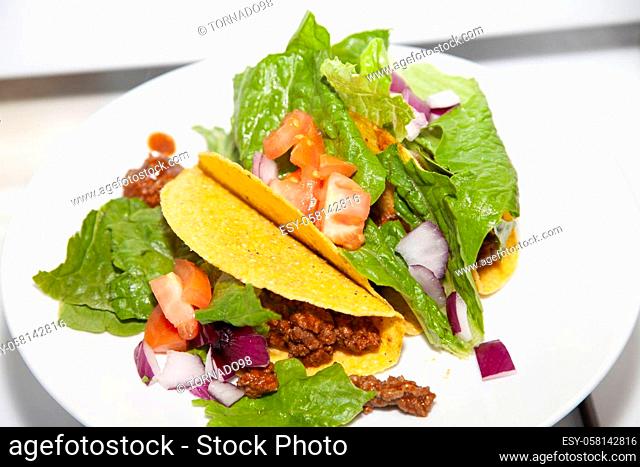 Three ground beef and salad tacos made with romaine lettuce, diced tomato and diced purple onion on a white plate