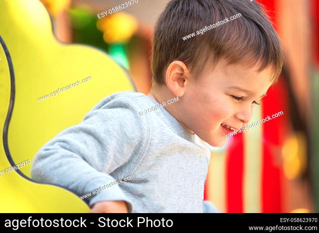 Cute happy baby boy with blond hair having fun on the playground on sunny summer day