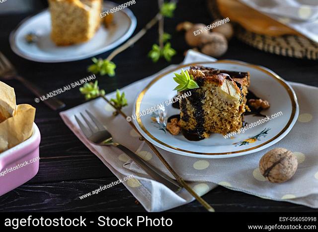 A piece of banana biscuit cake, poured with chocolate and decorated with walnuts and greens