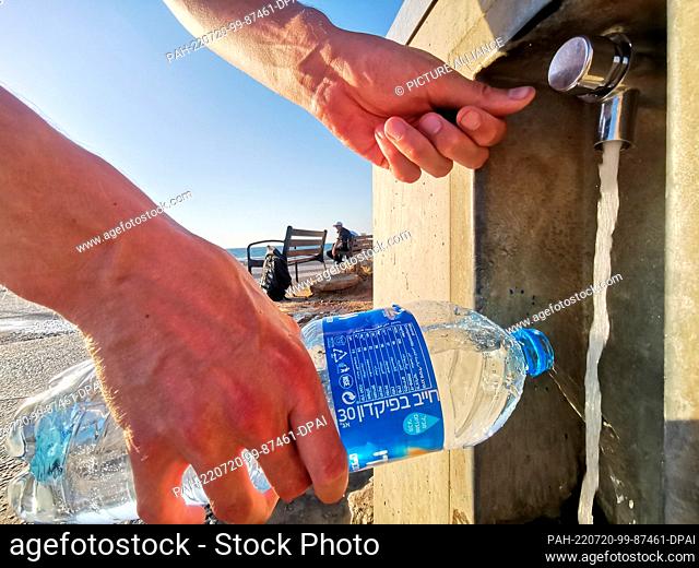 19 July 2022, Israel, Tel Aviv: A man fills a bottle with water at a drinking water dispenser on the mile-long beach promenade