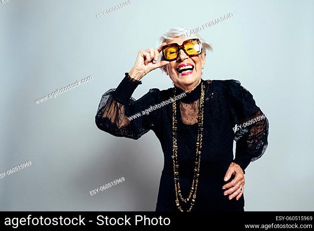 Beautiful and elegant old influencer woman. Cool grandmother posing in studio wearing fashionable clothes. Happy senior lady celebrating and making party
