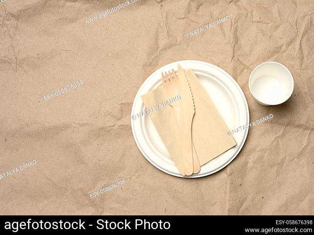 disposable round white paper plate and cup on brown paper background, top view
