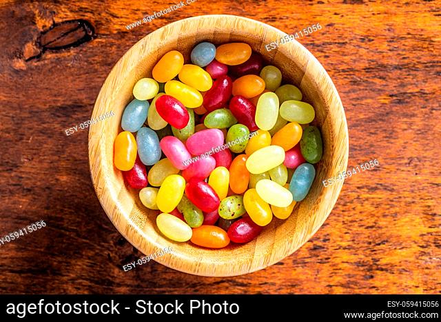 Sweet colorful jelly beans in wooden bowl on wooden table. Top view