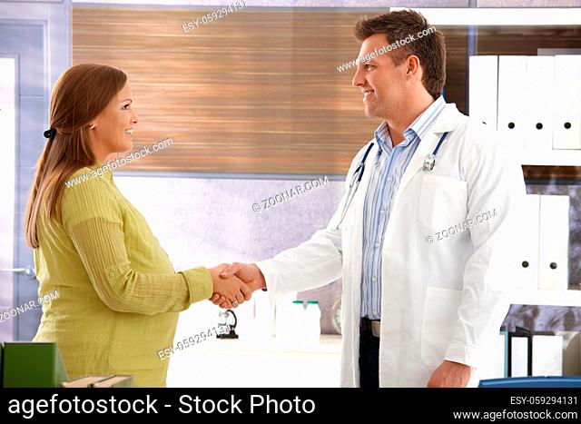 Smiling doctor shaking hands with pregnant woman in consulting room