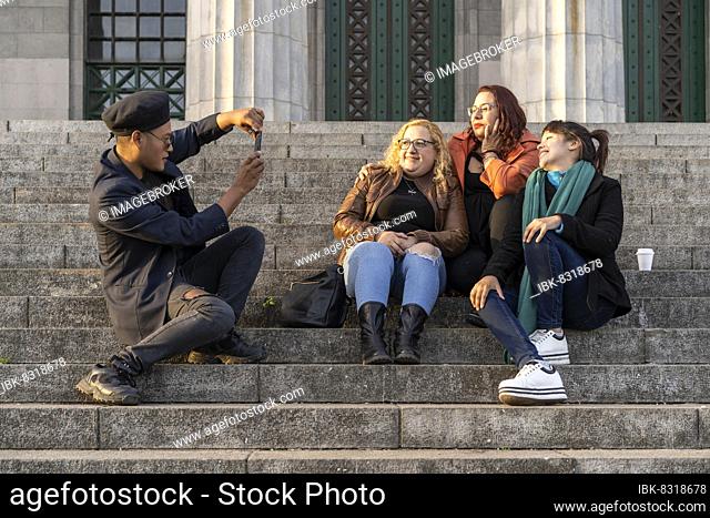 Multi ethnic group of friends sitting on some stairs having a good time chatting, laughing and taking photos